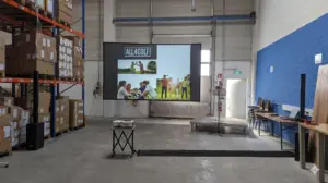 Professionelles Medientechnik-Setup von PvD - Events & Technik für eine Betriebsversammlung in einer Lagerhalle in Hannover, bestehend aus einer 4,60m Rahmenleinwand, lichtstarkem Beamer und Säulen-Lautsprechern.