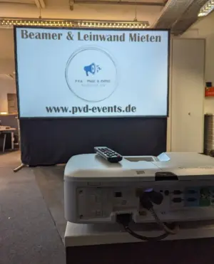 Lichtstarker 5000 Lumen Beamer auf einem Stativ-Tisch vor einer 3,1 Meter breiten Rahmenleinwand für Business-Events in OWL.