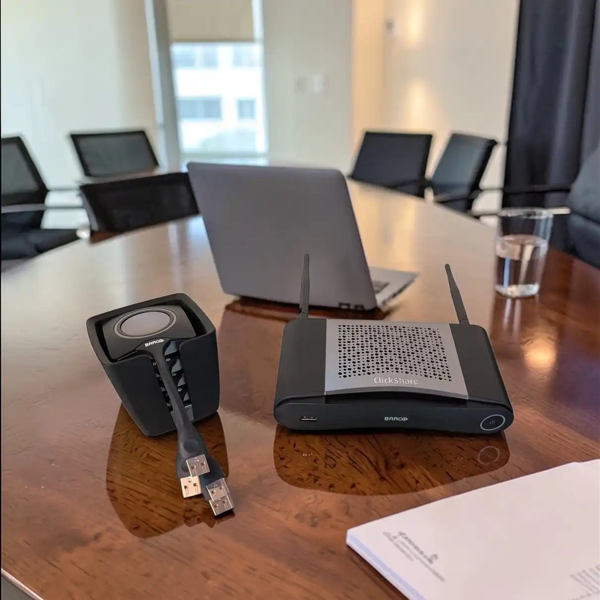 Barco ClickShare CSE-200 Base Unit mit USB-Buttons und Laptop auf einem Konferenztisch für kabellose Präsentationen.